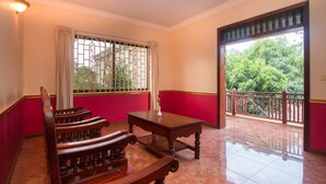 Una habitación con un banco de madera, una mesita y vistas a la vegetación a través de una ventana con barrotes.