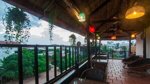 Un área de estar al aire libre con mesas y sillas, vista a la ciudad y plantas colgantes.