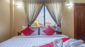 Habitación de hotel con cama, cortinas, ventana con vista a edificios y puerta de madera.