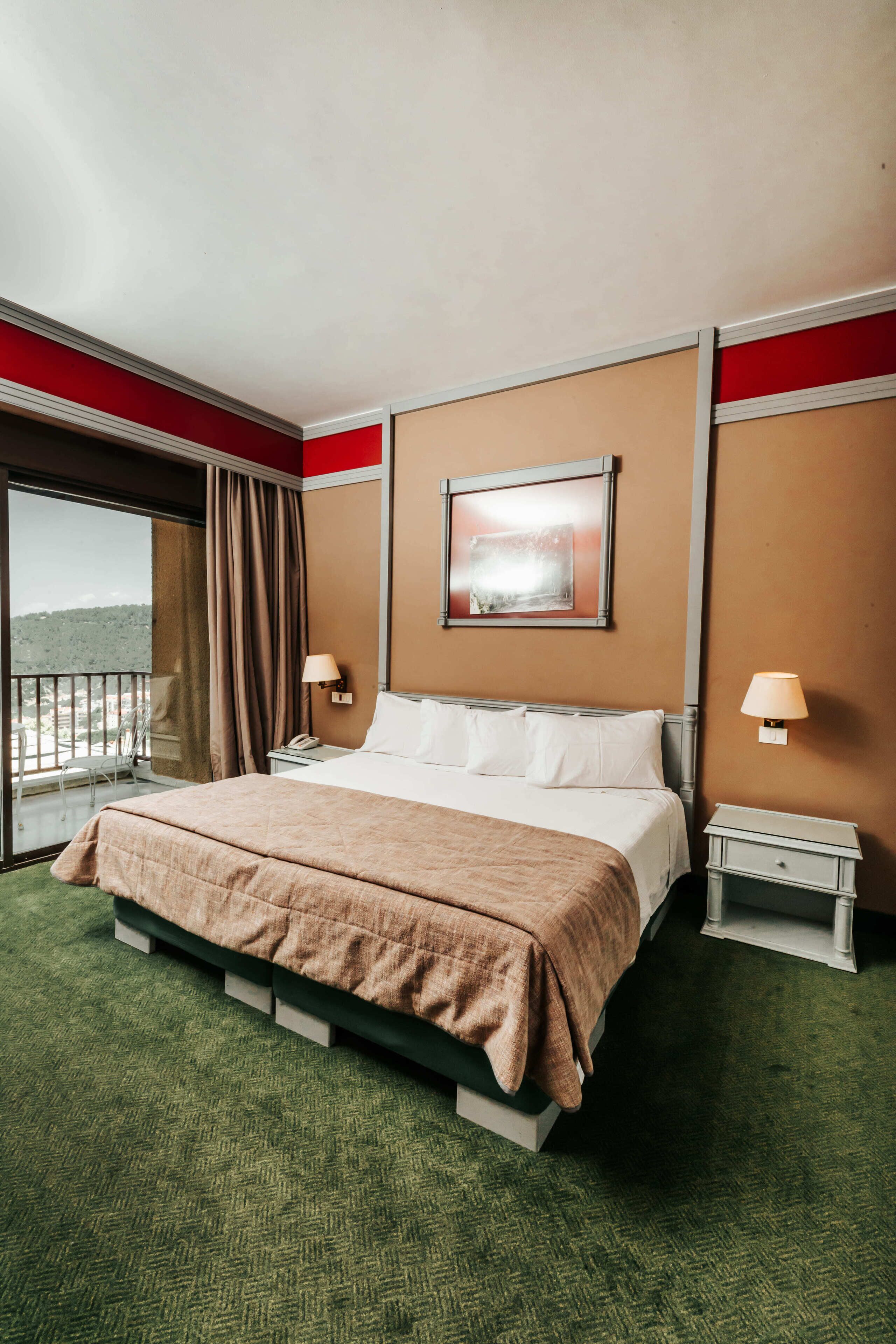 Une chambre d’hôtel avec un grand lit, deux tables de chevet, une fenêtre avec vue et un mur d’accent de couleur rouge.