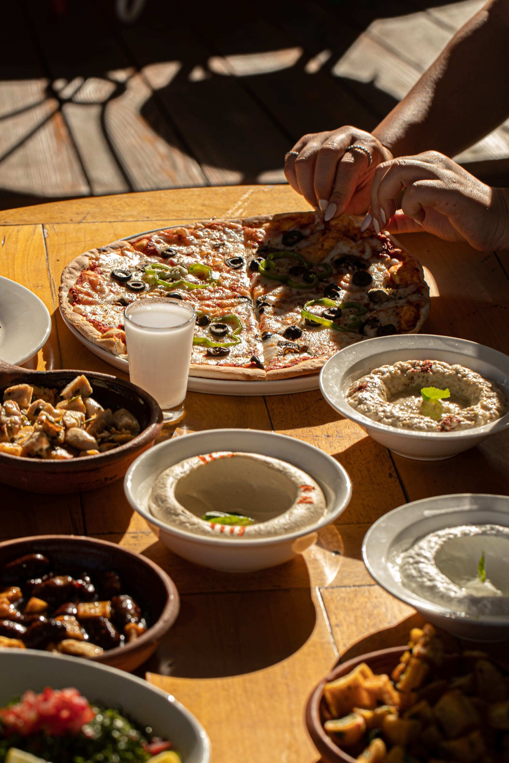 A table with a pizza, bowls of dips, and a glass of milk.