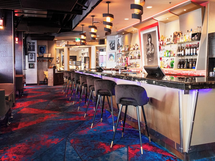Una zona de bar con una barra larga, varios taburetes y una alfombra estampada.