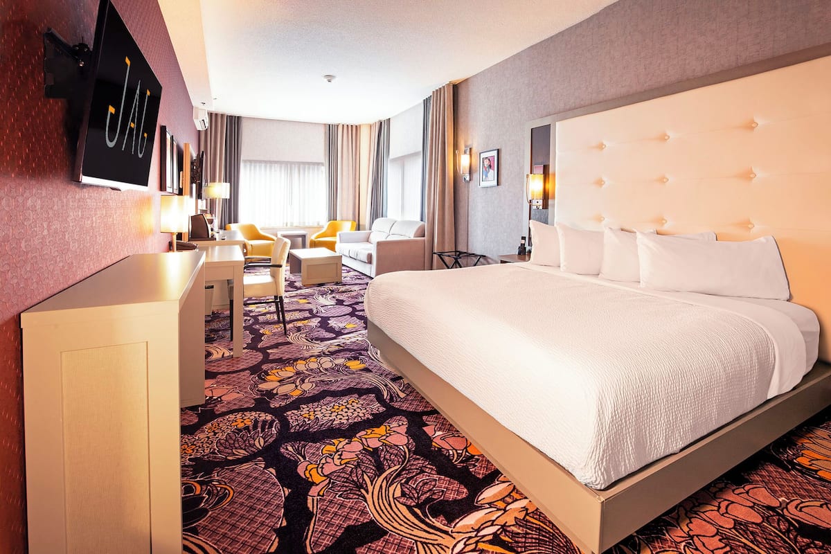 A hotel room with a large bed, a desk, a chair, and a television mounted on the wall.