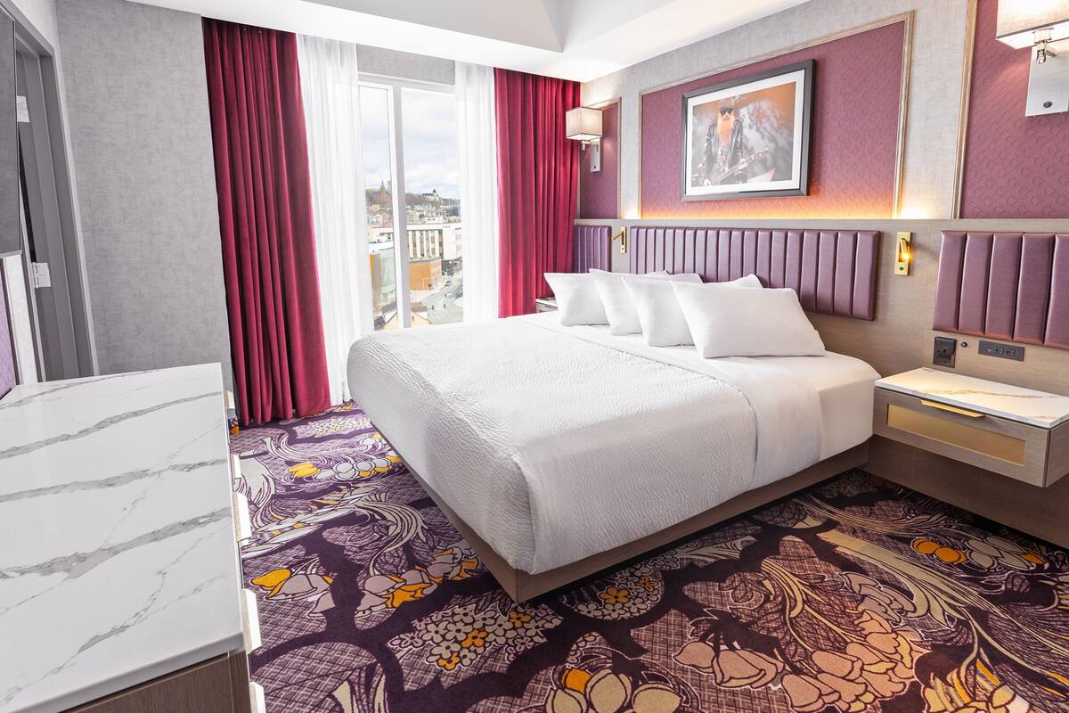 A hotel room with a large bed, a marble-topped desk, a patterned carpet, and a city view.