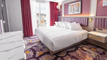 A hotel room with a large bed, a marble-topped desk, a patterned carpet, and a city view.