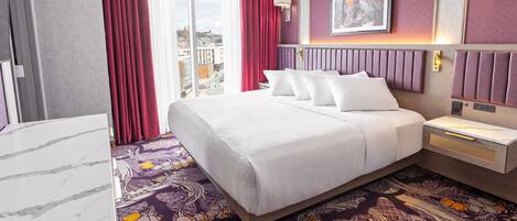 A hotel room with a large bed, a marble-topped desk, a patterned carpet, and a city view.