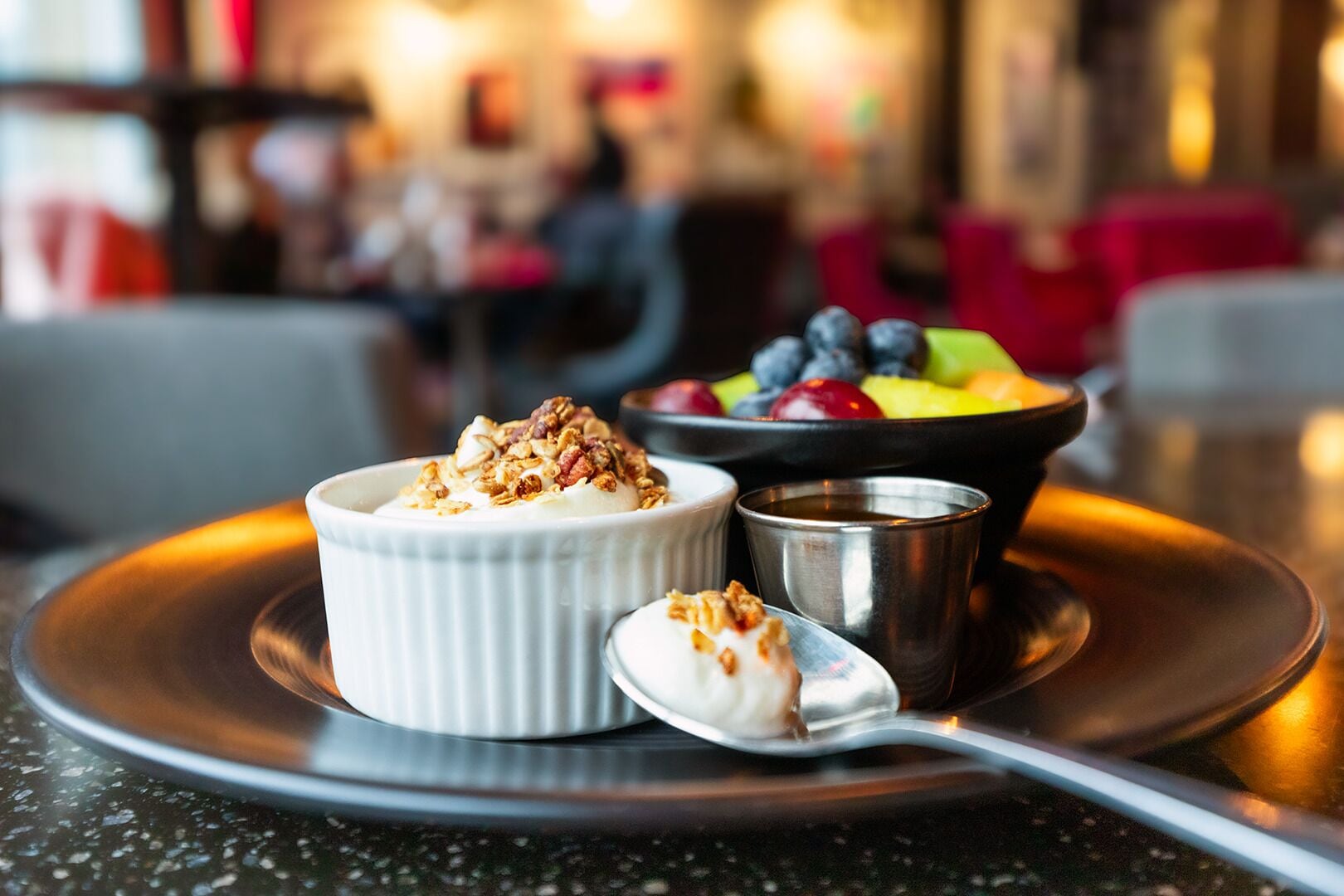 A dessert with a creamy topping and granola, a bowl of mixed berries, and a small metal cup on a plate.