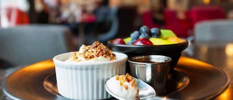 A dessert with a creamy topping and granola, a bowl of mixed berries, and a small metal cup on a plate.