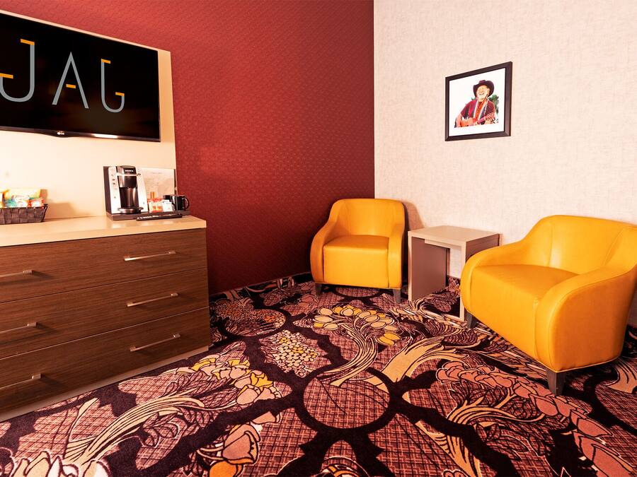 A hotel room with a dark wooden dresser, a coffee maker, a framed picture on the wall, and two yellow armchairs.
