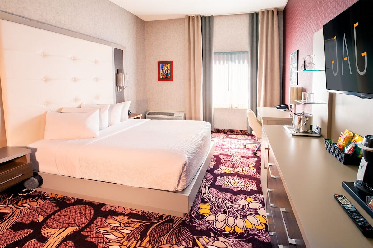 A hotel room with a large bed, a desk with a computer, a flat-screen TV, and a minibar.