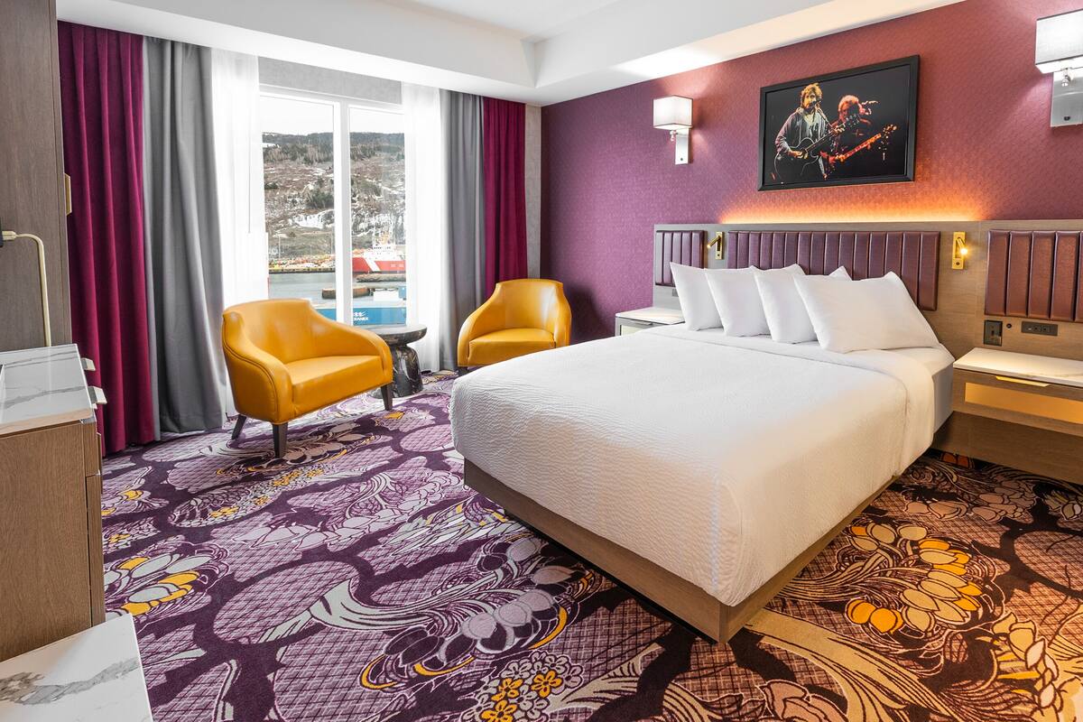 A hotel room with a large bed, two armchairs, a small table, and a view of a snowy landscape through the window.