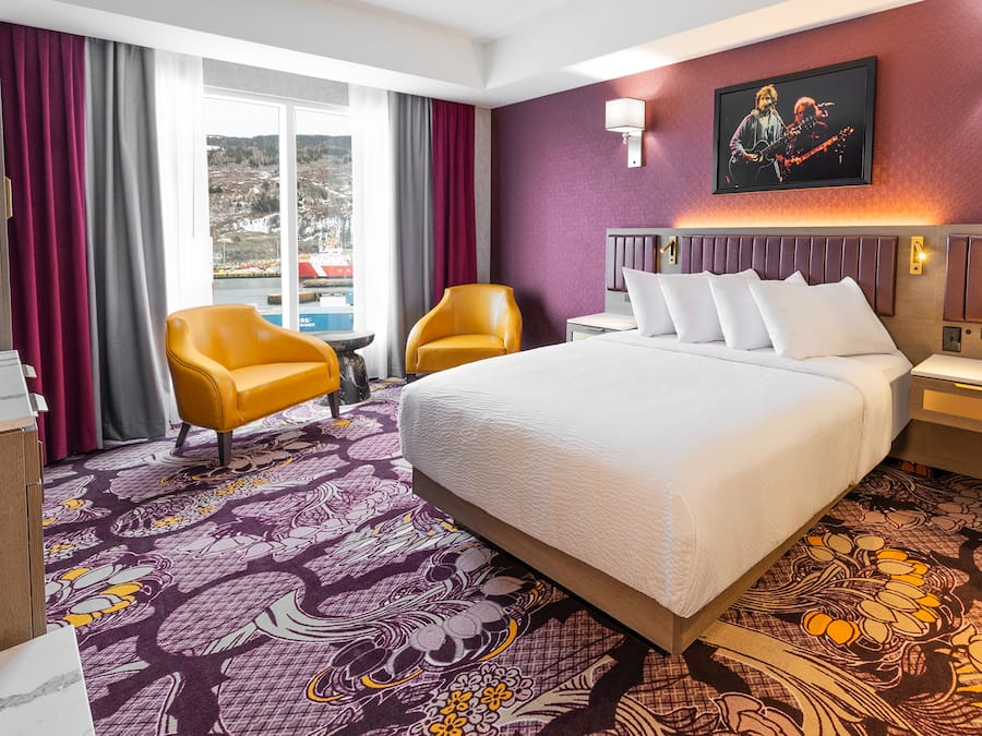 A hotel room with a large bed, two armchairs, a small table, and a view of a snowy landscape through the window.