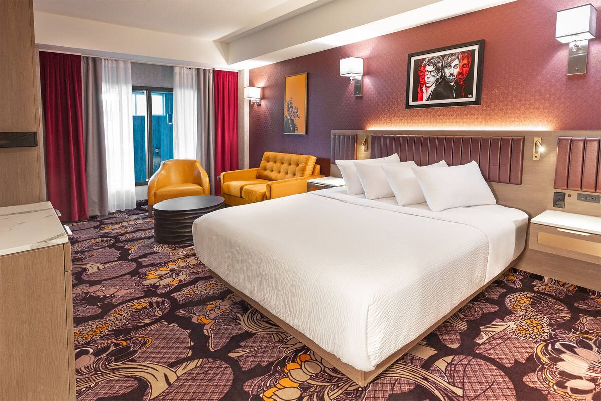 A hotel room with a large bed, a sofa, a chair, a desk, and a window with curtains.