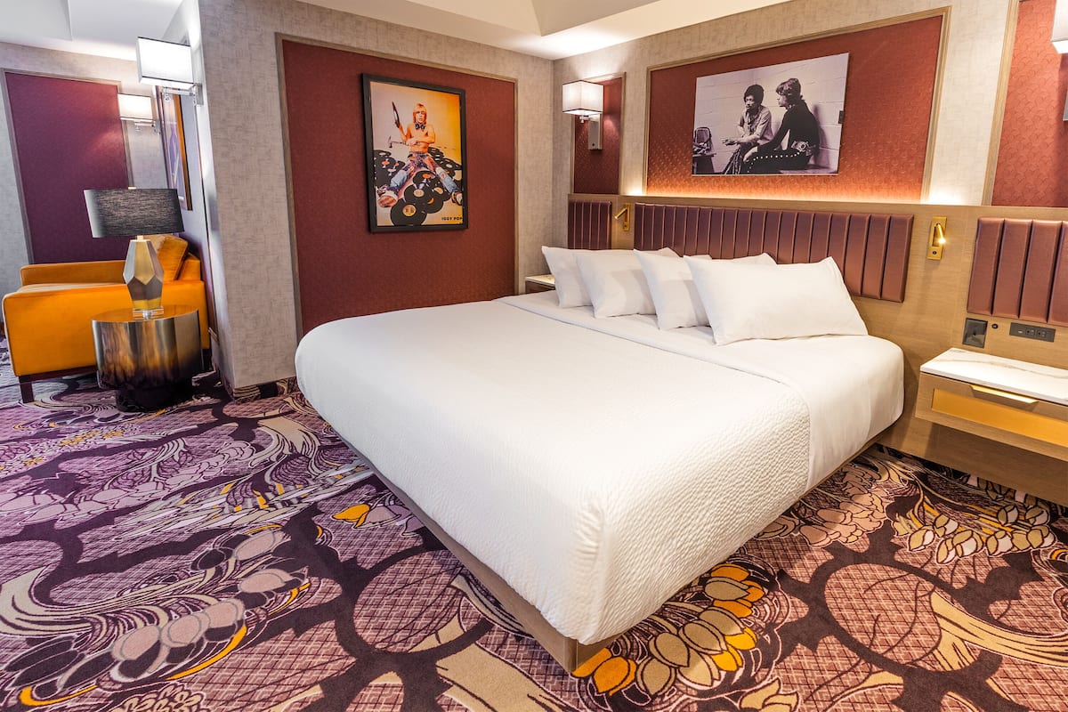 A hotel room with a large bed, a bedside table, a chair, and a decorative rug.