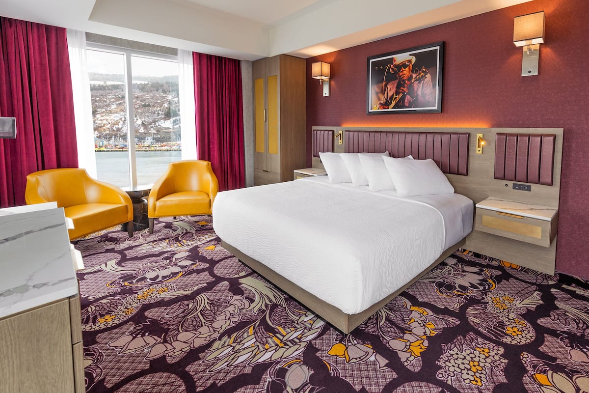 A hotel room with a large bed, a desk, a chair, and a view of a cityscape through the window.