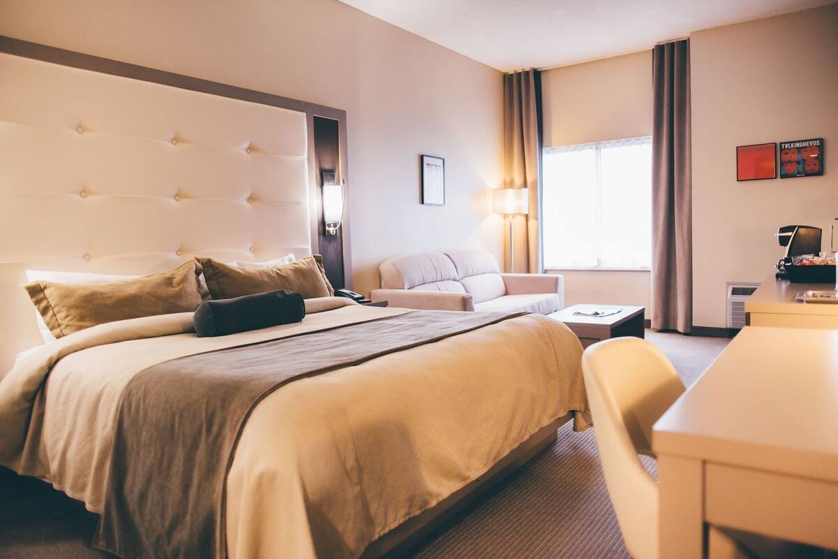 A hotel room with a large bed, a sofa, a desk, and a window with curtains.