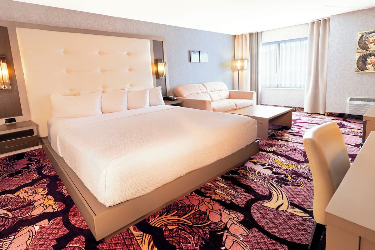 A hotel room with a large bed, a sofa, a desk, and a patterned carpet.