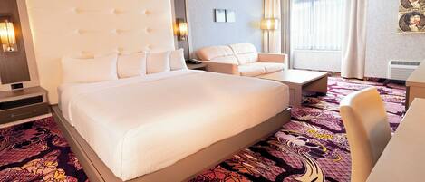 A hotel room with a large bed, a sofa, a desk, and a patterned carpet.
