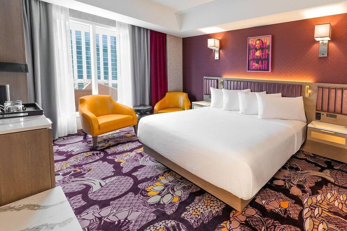 A hotel room with a large bed, two chairs, a desk, and a window with curtains.