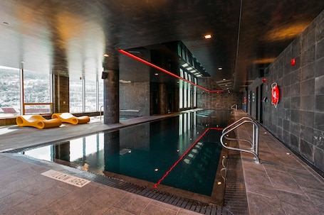 An indoor swimming pool with clear water, a red safety line, and yellow lounge chairs.. Jag Boutique Hotel