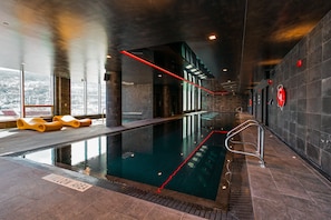 An indoor swimming pool with clear water, a red safety line, and yellow lounge chairs.