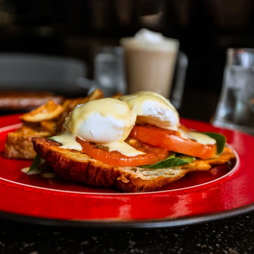 Un plato de desayuno con huevos Benedict, tostadas, tomate y verduras de hoja.