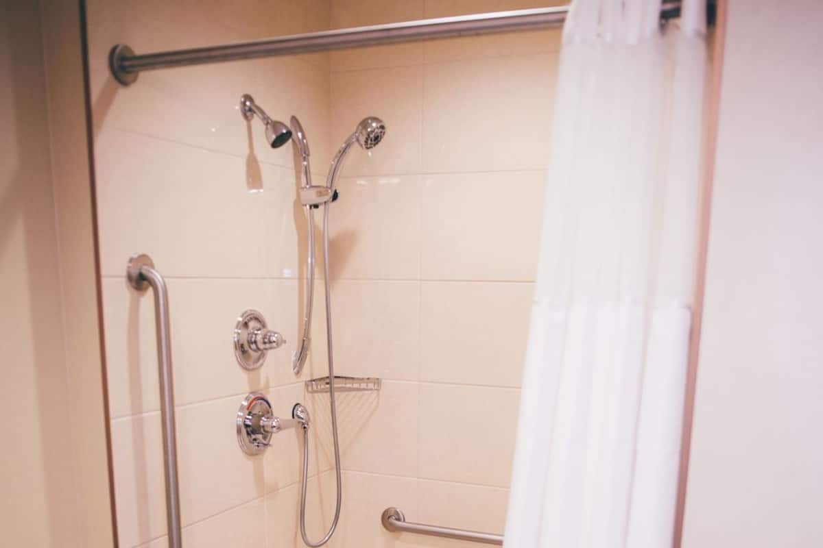 A shower with a grab bar, a handheld showerhead, and a shower curtain.