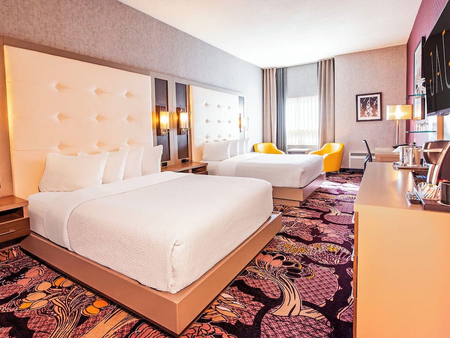 A hotel room with a large bed, two bedside tables, a desk, a chair, and a television.
