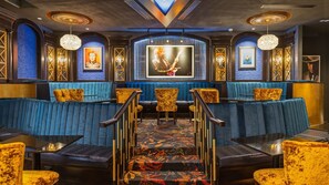 A bar area with blue upholstered seating, gold-framed artwork, and a patterned carpet.