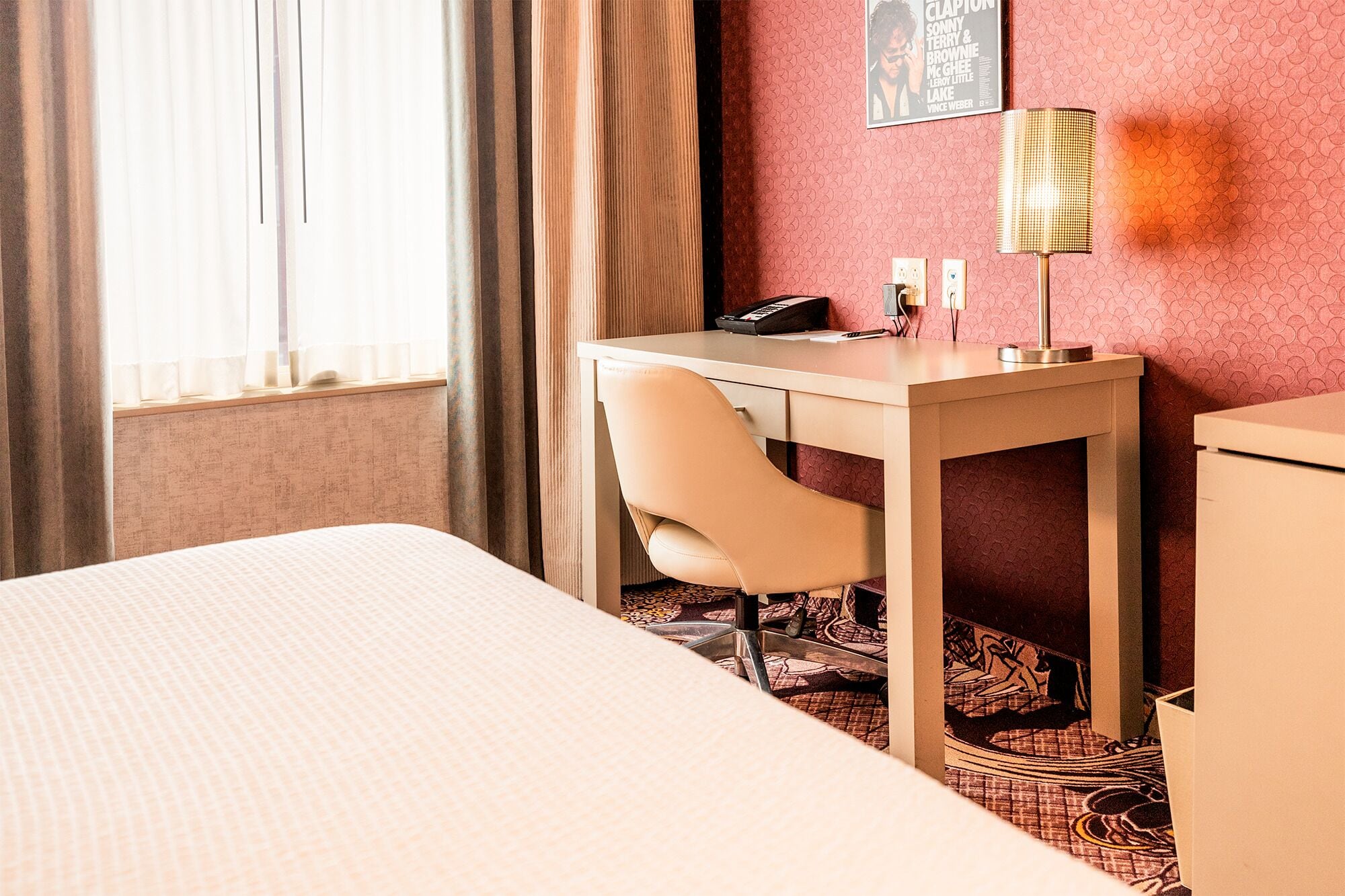 Een hotelkamer met een bed, een bureau, een stoel, een lamp en een telefoon.
