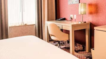 A hotel room with a bed, a desk, a chair, a lamp, and a telephone.