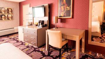 Camera d'albergo con un letto, una scrivania, una sedia, una televisione, una macchina del caffè e uno specchio.