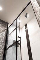 A modern shower with a glass door and a ceiling-mounted rain showerhead.