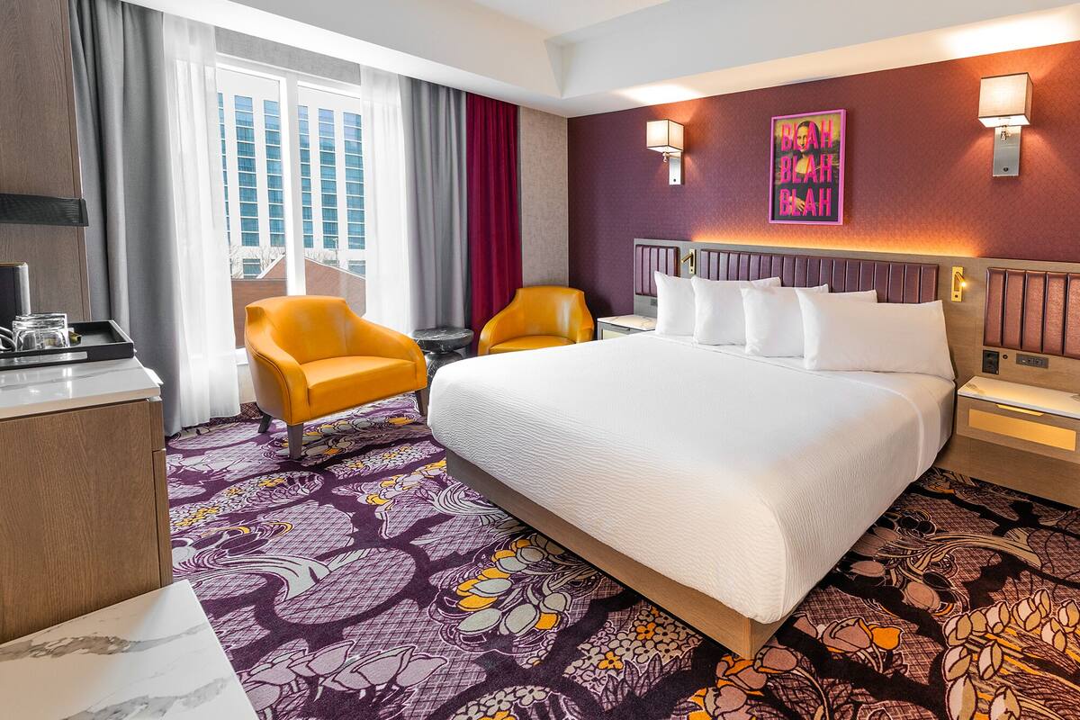 A hotel room with a large bed, two chairs, a desk, and a window with curtains.