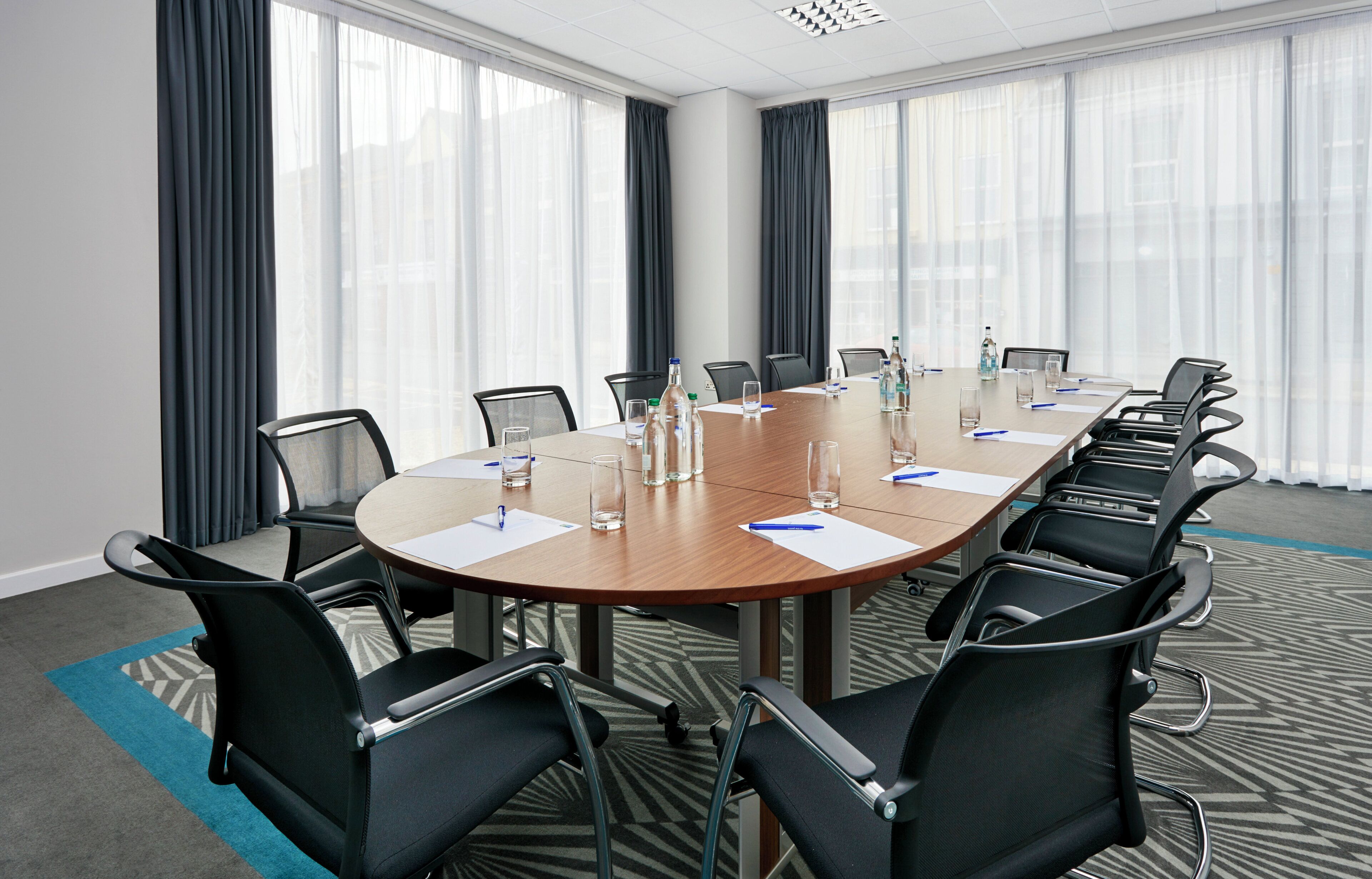Sala de conferência com mesa redonda, cadeiras e piso coberto por carpete.