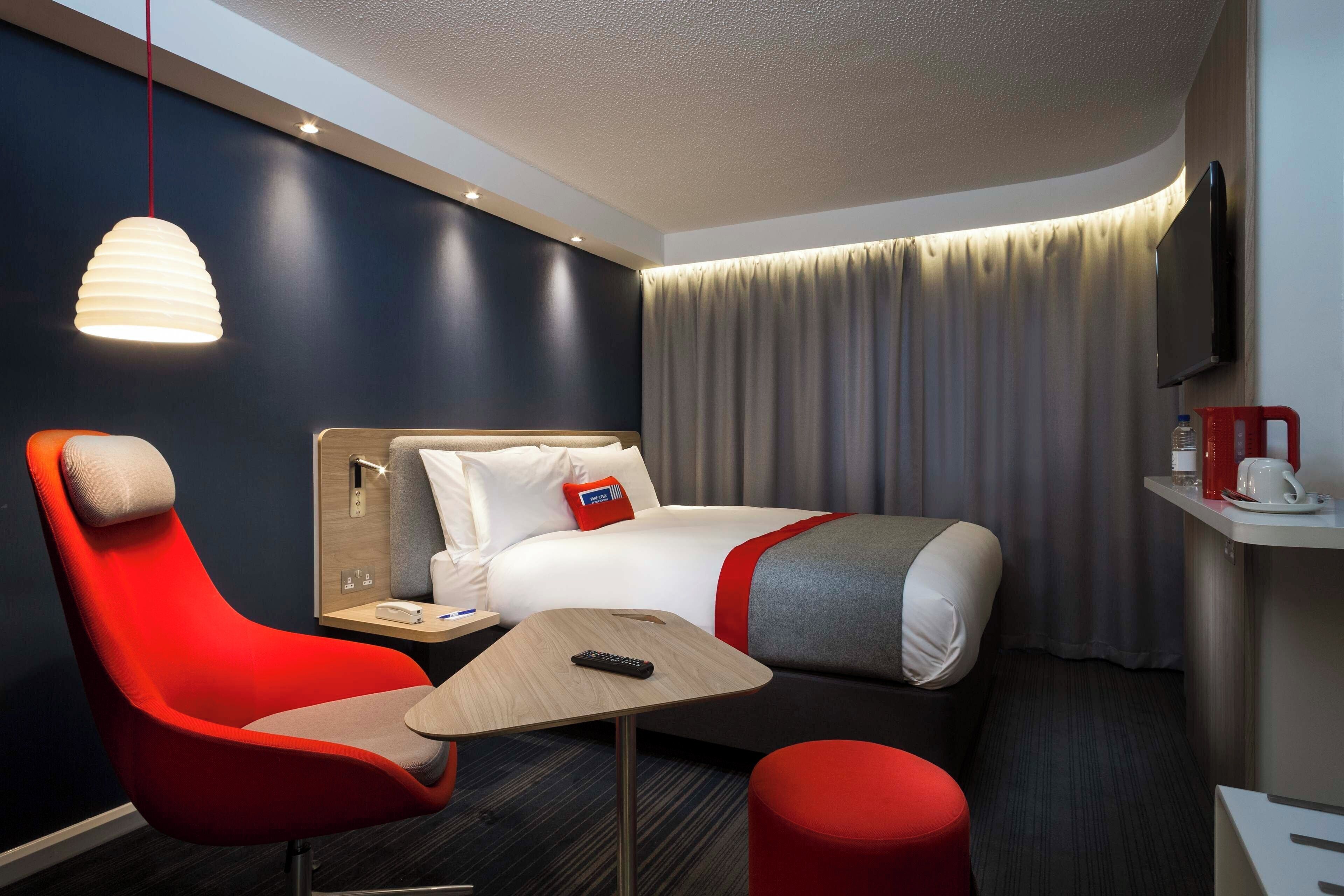 A hotel room with a bed, a desk, a chair, a TV, and a window with curtains.