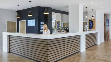 A hotel reception area with a modern design, featuring a reception desk, a bar area, and a counter with various amenities.