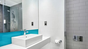 Een moderne badkamer met een witte wastafel, een blauwe accentmuur en een douche met glazen wanden.