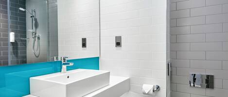 A modern bathroom with a white sink, blue accent wall, and a glass-enclosed shower.