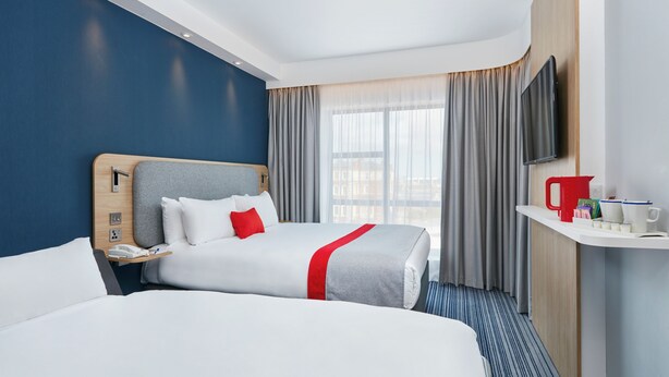 Een hotelkamer met twee bedden, een televisie, een nachtkastje met telefoon en een raam met gordijnen.
