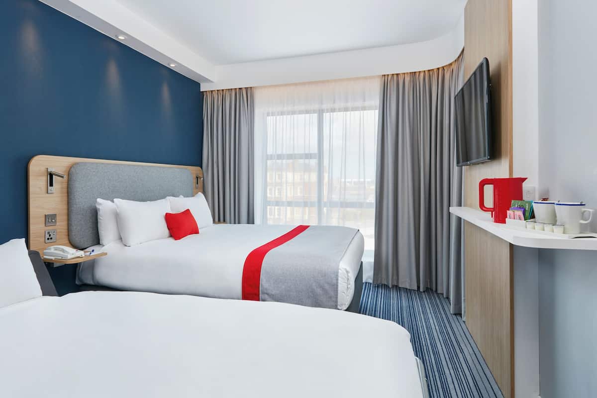 A hotel room with two beds, a TV, a bedside table with a phone, and a window with curtains.