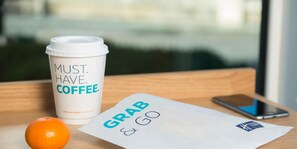 A coffee cup with "MUST HAVE COFFEE" text, a smartphone, and a piece of paper with "GRAB & GO" text on a wooden surface. - Holiday Inn Express Grimsby by IHG (Grimsby)