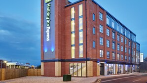 Um hotel Holiday Inn Express com fachada de tijolos, grandes janelas e entrada visível.