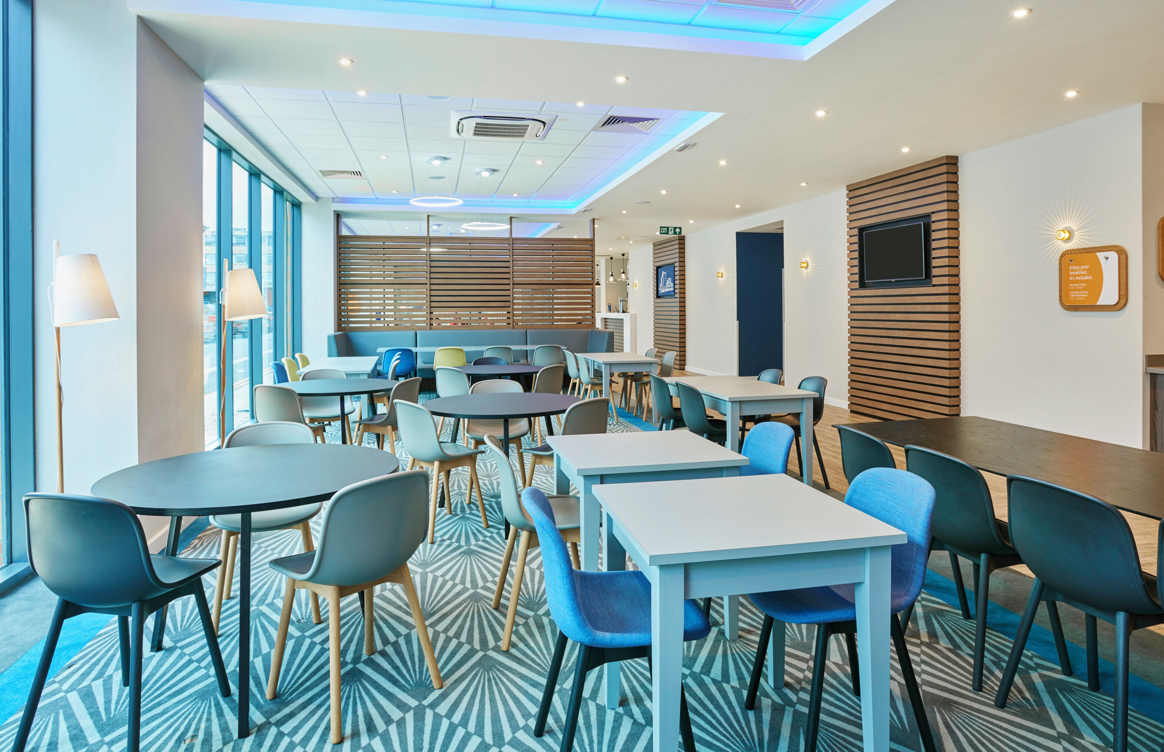 A modern dining area with round tables and chairs, a patterned floor, and a view of the city through large windows.