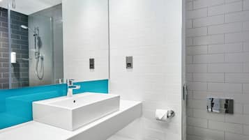 Uma casa de banho moderna com uma sanita, chuveiro, lavatório e espelho.