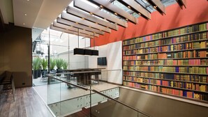 Interior de una biblioteca moderna con barandilla de cristal, suelo de madera y una amplia estantería llena de libros.