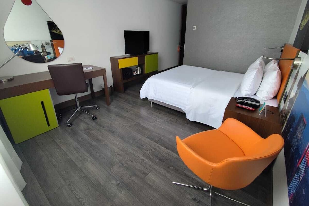 A hotel room with a bed, a desk with a chair, a TV, and a mirror.
