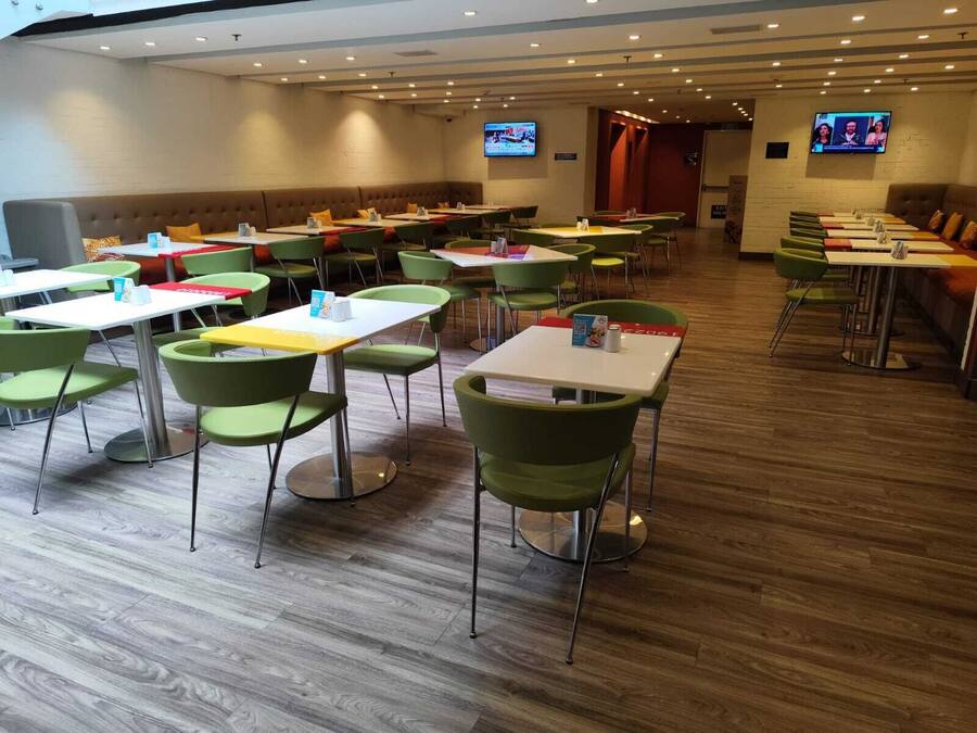 Un comedor de hotel con varias mesas y sillas, piso de madera y dos televisores en las paredes.