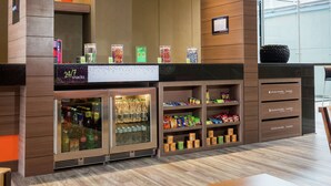 Un bar de aperitivos con un mostrador refrigerado, estantes llenos de provisiones y un letrero que indica servicio las 24 horas.