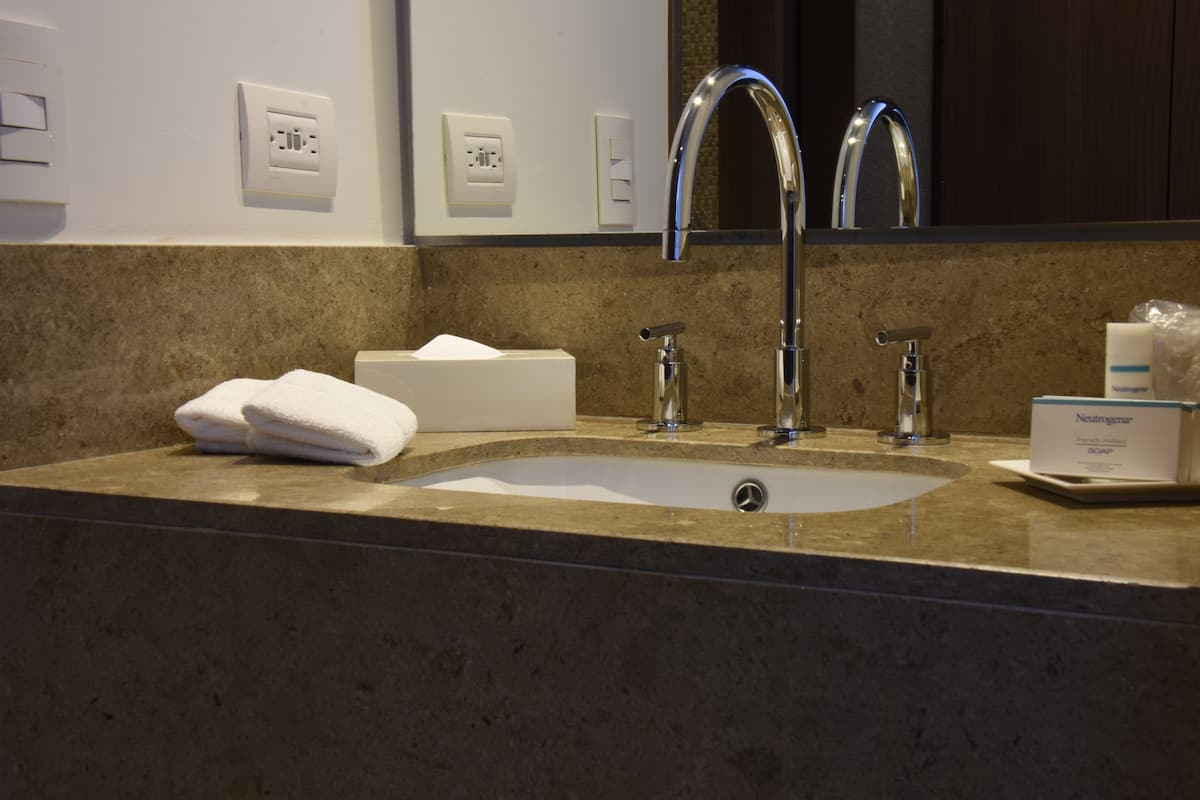 A bathroom with a sink, two faucets, a towel, and a soap dispenser.